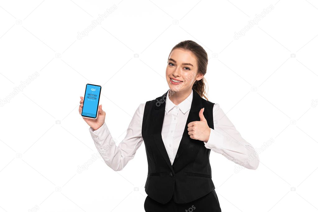 KYIV, UKRAINE - APRIL 7, 2019: happy young waitress holding smartphone with skype app and showing thumb up isolated on white