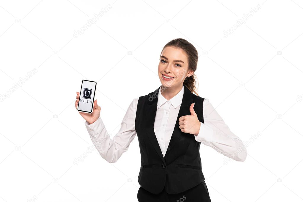 KYIV, UKRAINE - APRIL 7, 2019: happy young waitress holding smartphone with uber app and showing thumb up isolated on white