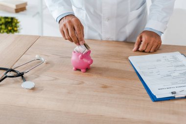 Pano ve stetoskop yakın domuzcuk bankada dolar banknot koyarak beyaz ceket adam kırpılmış görünümü 