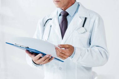 cropped view of doctor in white coat holding page and clipboard in clinic  clipart