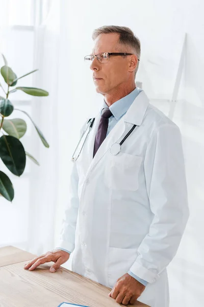 Szép Orvos Fehér Kabátot Szemüveg Állandó Közelében Íróasztal — Stock Fotó