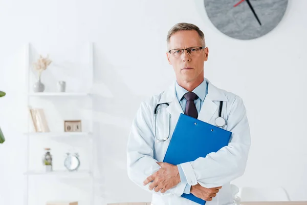 Ernsthafter Arzt Mit Brille Steht Und Hält Klemmbrett Während Die — Stockfoto