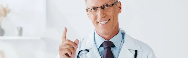 クリニックで指を指差す眼鏡で幸せな男のパノラマショット — ストック写真