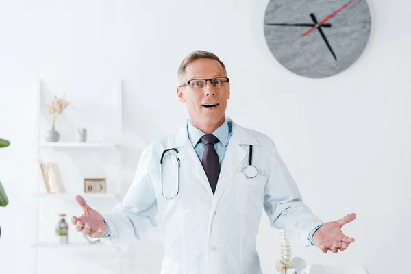 Zaskoczony Lekarz Białym Płaszczu Okulary Wskazując Klinice — Zdjęcie stockowe