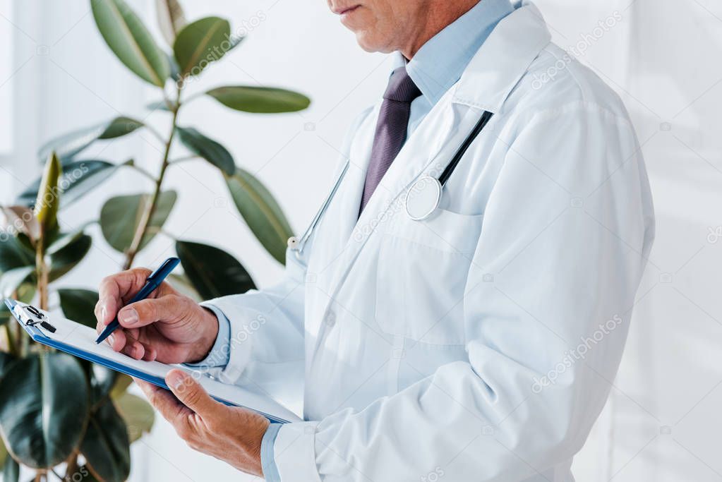 cropped view of man in white coat writing diagnosis and holding clipboard 