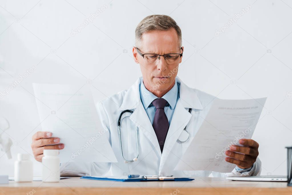 doctor in glasses and white coat with stethoscope looking at documents 