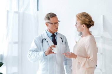 Doktor içinde gözlük tutarak şişe yakın kadın işaret ile klinik parmak 