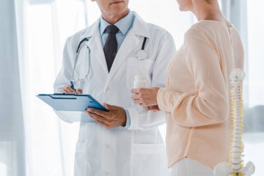 cropped view of doctor holding clipboard and pen near woman with bottle  clipart