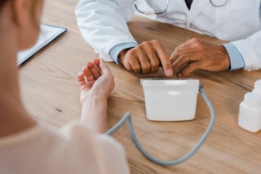 selective focus of doctor pushing button while measuring blood pressure of woman  clipart