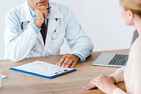 обрезанный вид доктора, держащего ручку и сидящего рядом с женщиной
 