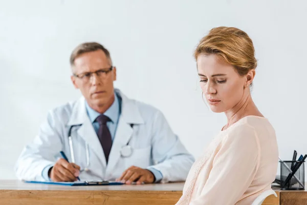 白いコートを着て医者の近くに座っている悲しい女性の選択的な焦点 — ストック写真