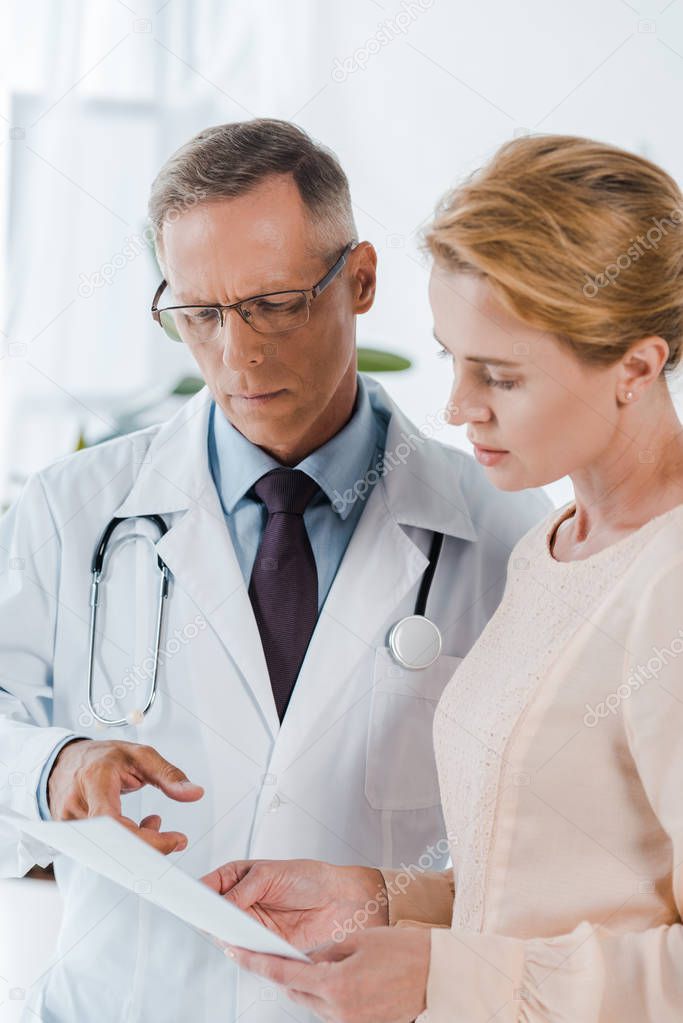 doctor in glasses pointing with finger at document near woman 