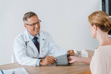 selective focus of happy doctor measuring blood pressure of woman  clipart