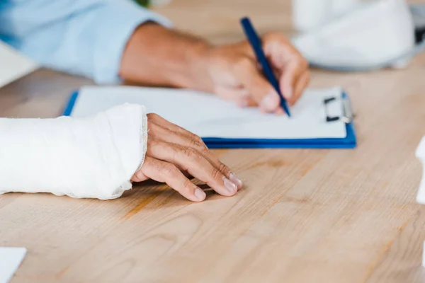 Cropped View Injured Man Gypsum Bandage Broken Arm Writing Clipboard — Stock Photo, Image