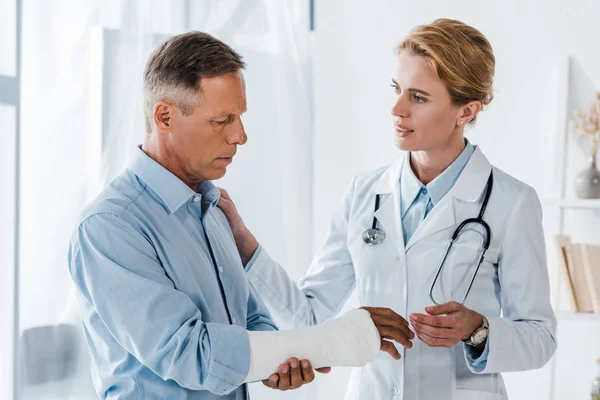 Attraente Medico Guardando Uomo Con Braccio Rotto Clinica — Foto Stock