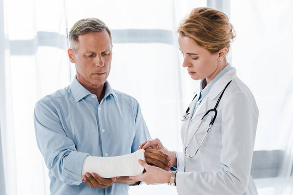 attractive doctor touching broken arm on handsome man in clinic 