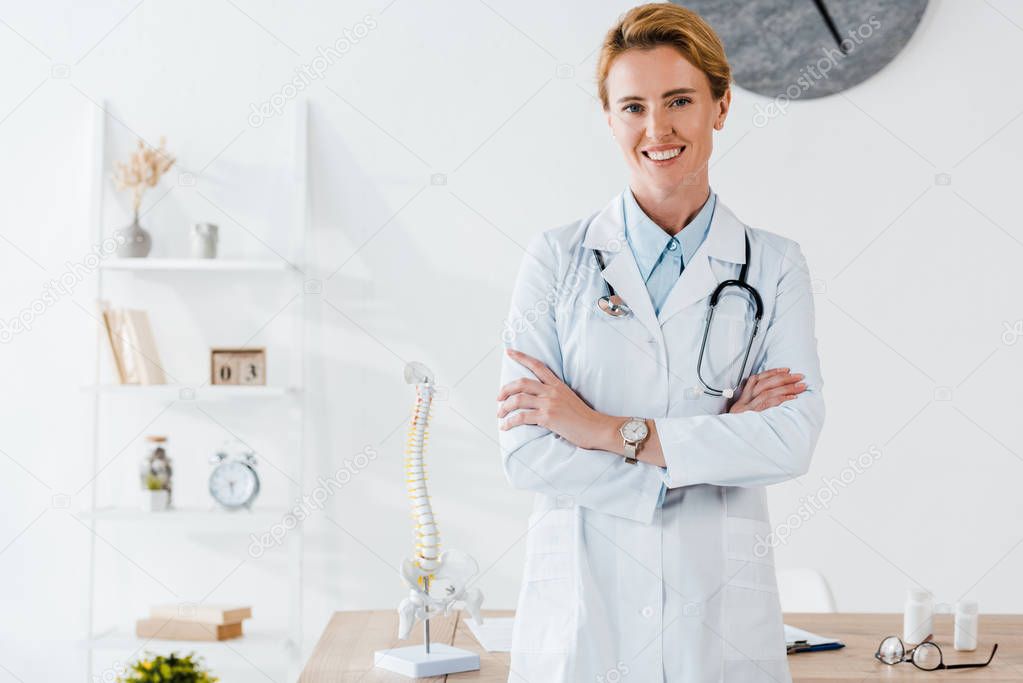 attractive and positive doctor standing with crossed arms in clinic 