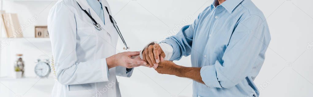 panoramic shot of doctor touching broken arm on man in clinic 