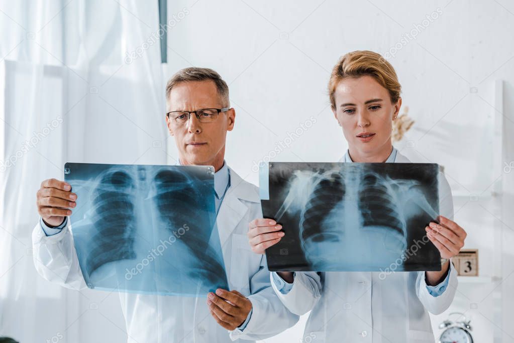doctor in glasses and attractive coworker looking at x-rays in clinic 