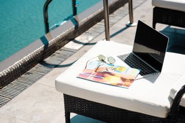 laptop with blank screen, magazine and sunglasses on sun bed near swimming pool clipart