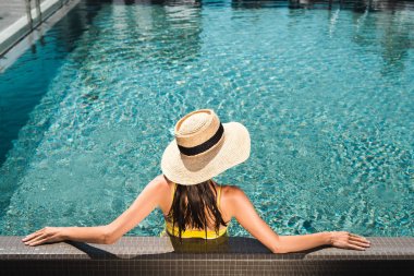 back view on woman in straw hat relaxing in swimming  pool clipart