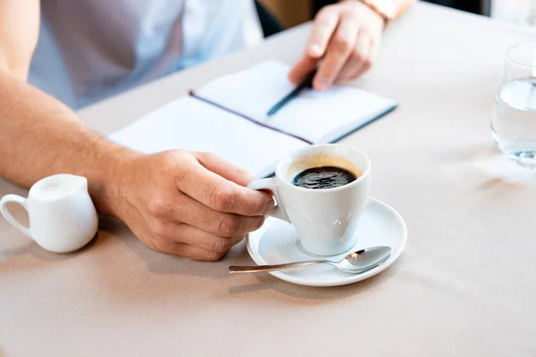 Частичный Вид Человека Держащего Чашку Кофе Сидящего Кафе Учебником Ручкой — стоковое фото