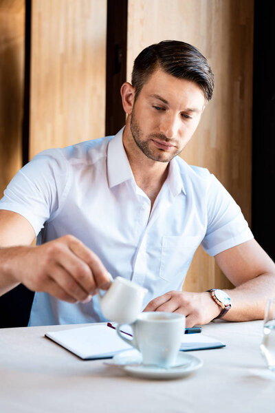 сфокусированный мускулистый мужчина наливает сливки в кофе в кафе
