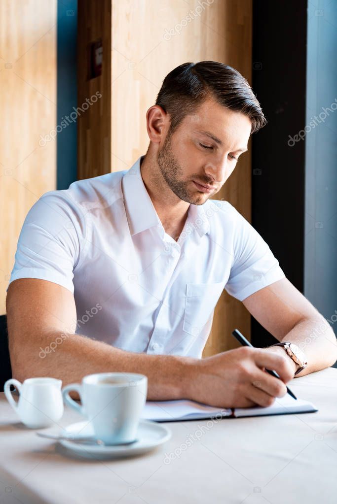 focused handsome man writing in textbook in cafe