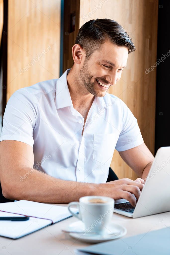 smiling freelancer typing on laptop keyboard in cafe