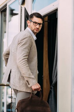 gözlük ciddi işadamı deri çanta tutan ve kamera bakarak