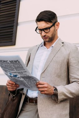focused businessman in glasses reading newspaper on street clipart