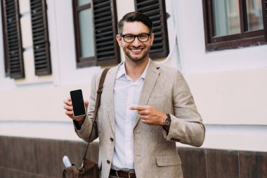 sokakta boş ekran ile akıllı telefon parmak ile işaret gülümseyen işadamı ön görünümü