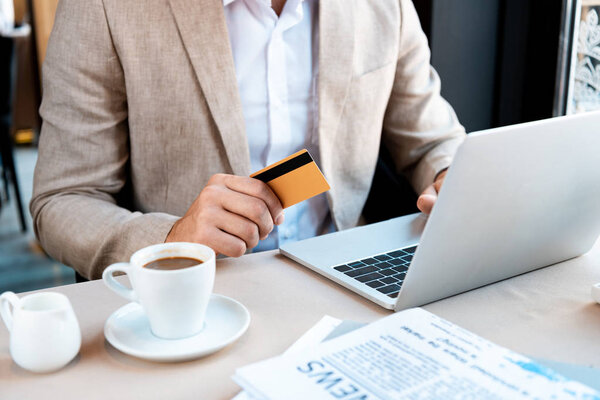cropped view of businessman with credit card and laptop in cafe