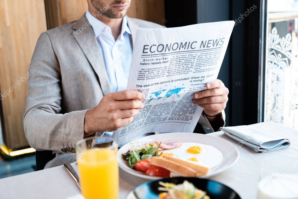 businessman sitting at served table and reading newspaper in cafe