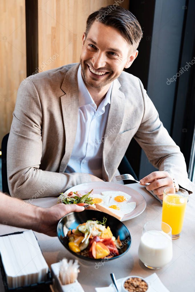 businessman smiling while waiter putting dish on table in cafe