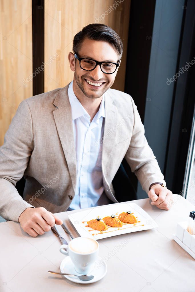 smiling businessman in glasses sitting at table with delicious dish in cafe