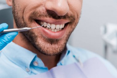 cropped view of dentist holding dental instrument near cheerful man  clipart