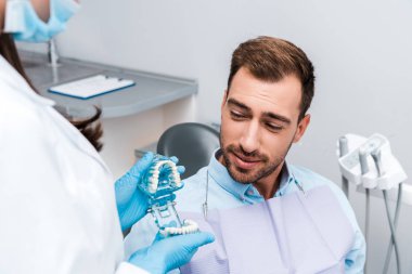yakışıklı hasta yakın diş modeli tutan medial maske ve lateks eldiven diş hekimi kırpılmış görünümü 