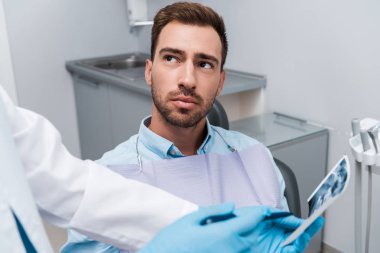 cropped view of dentist holding x-ray near handsome patient  clipart