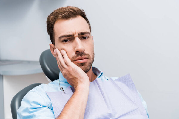 upset bearded man touching face while having toothache in dental clinic 