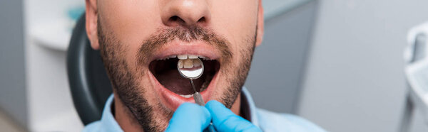 panoramic shot of dentist holding dental mirror in mouth of bearded patient 