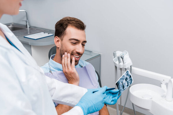 selective focus of cheerful man looking at x-ray near dentist in white coat 