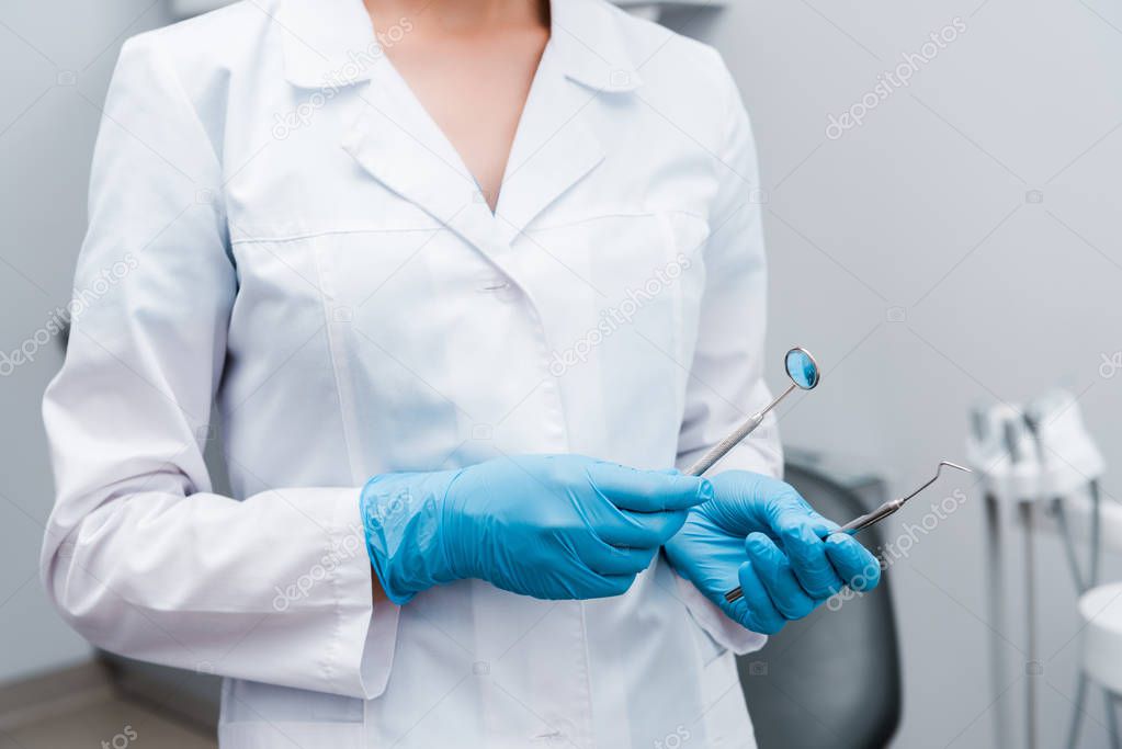cropped view of dentist in blue latex gloves holding stainless medical instruments 
