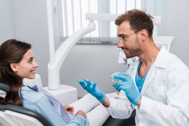 gözlük neşeli diş hekimi diş modeli tutan ve mutlu kadın bakıyor 