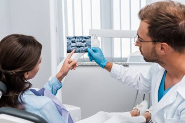 bearded dentist in latex glove holding x-ray near patient  clipart