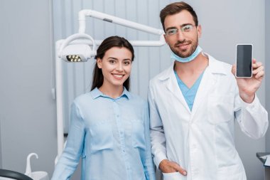 boş ekranlı akıllı telefonu cepte eliyle dişçinin yanında duran neşeli kız 