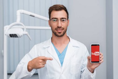 Kiev, Ukrayna - 10 Temmuz 2019: ekranda youtube uygulaması ile akıllı telefon parmak ile işaret beyaz ceketli yakışıklı sakallı adam 