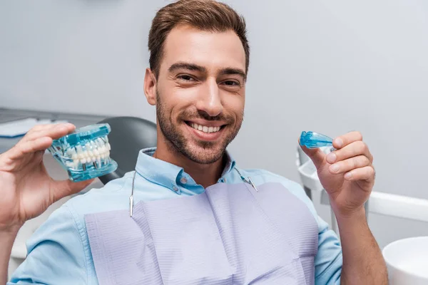 快乐胡子的男人拿着固定器和牙齿模型在手中 — 图库照片