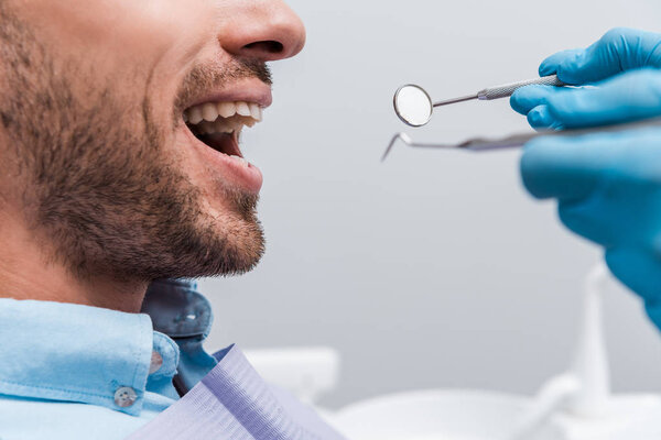 cropped view of woman in latex gloves holding dental instruments near patient 