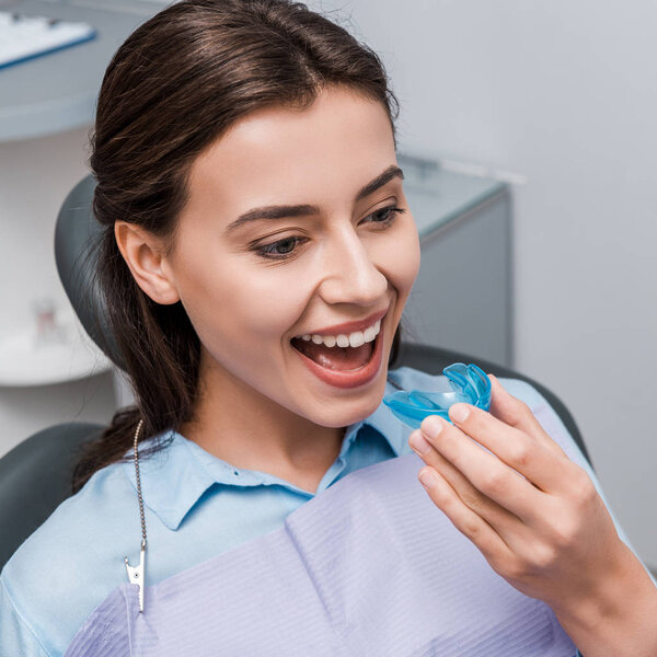 happy woman holding blue retainer in dental clinic 